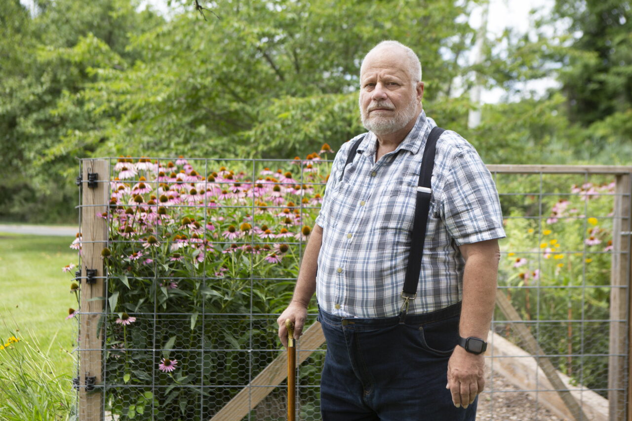 Jeff La Marca stands outdoors, with pink flowers and trees in the background.