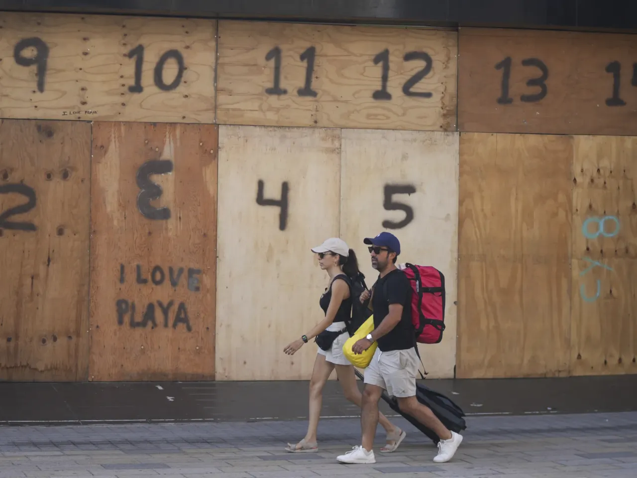 People walk past a souvenir shop's storefront boarded up preparation for the arrival of Hurricane Beryl, in Playa del Carmen, Mexico, Thursday, July 4, 2024.
