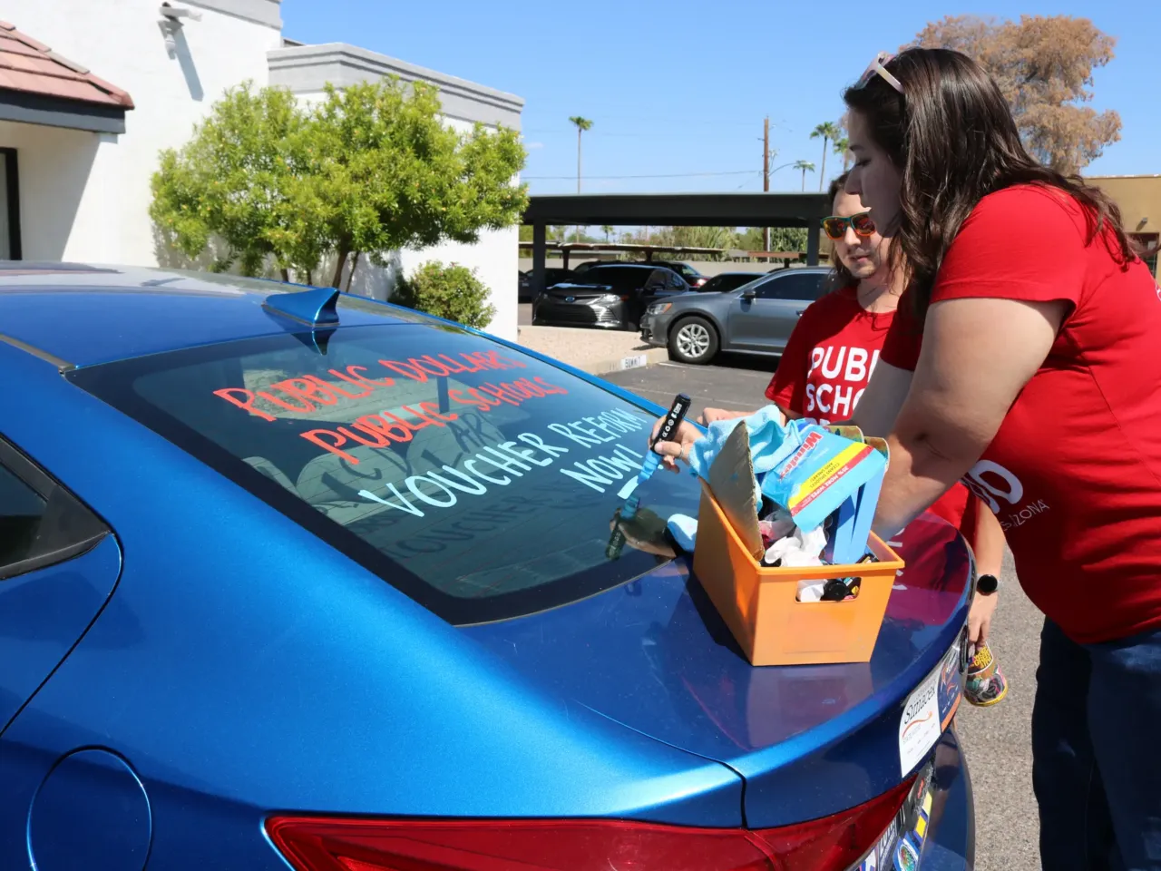 Jen Senatore, right, and Tyler Kowch with Save Our Schools, a public education advocacy group in Arizona, paint cars outside of a local Democratic Party office in Phoenix. The paint reads, "Voucher reform now!"