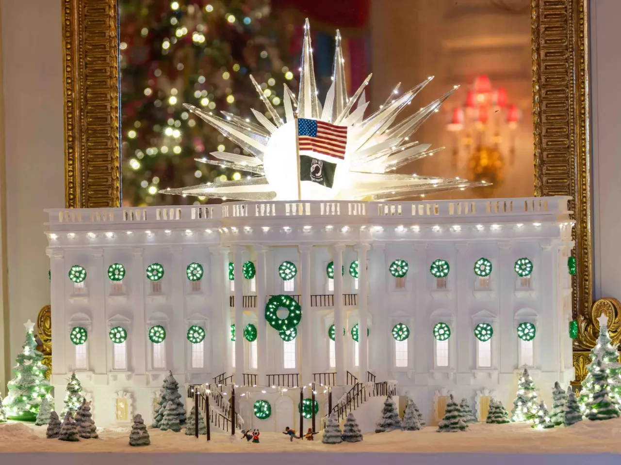 A starburst made out of sugar shines above the massive gingerbread White House in the State Dining Room, which includes snow-covered South Grounds dotted with dozens of twinkling mini Christmas trees and a scene of people ice skating in a rink on the South Lawn.