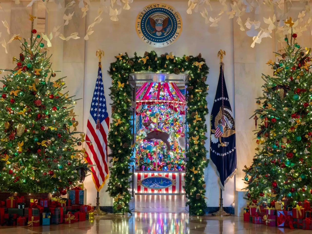 Decorated trees in the Cross Hall frame the door to the Blue Room. Doves are also suspended overhead along the Cross Hall.