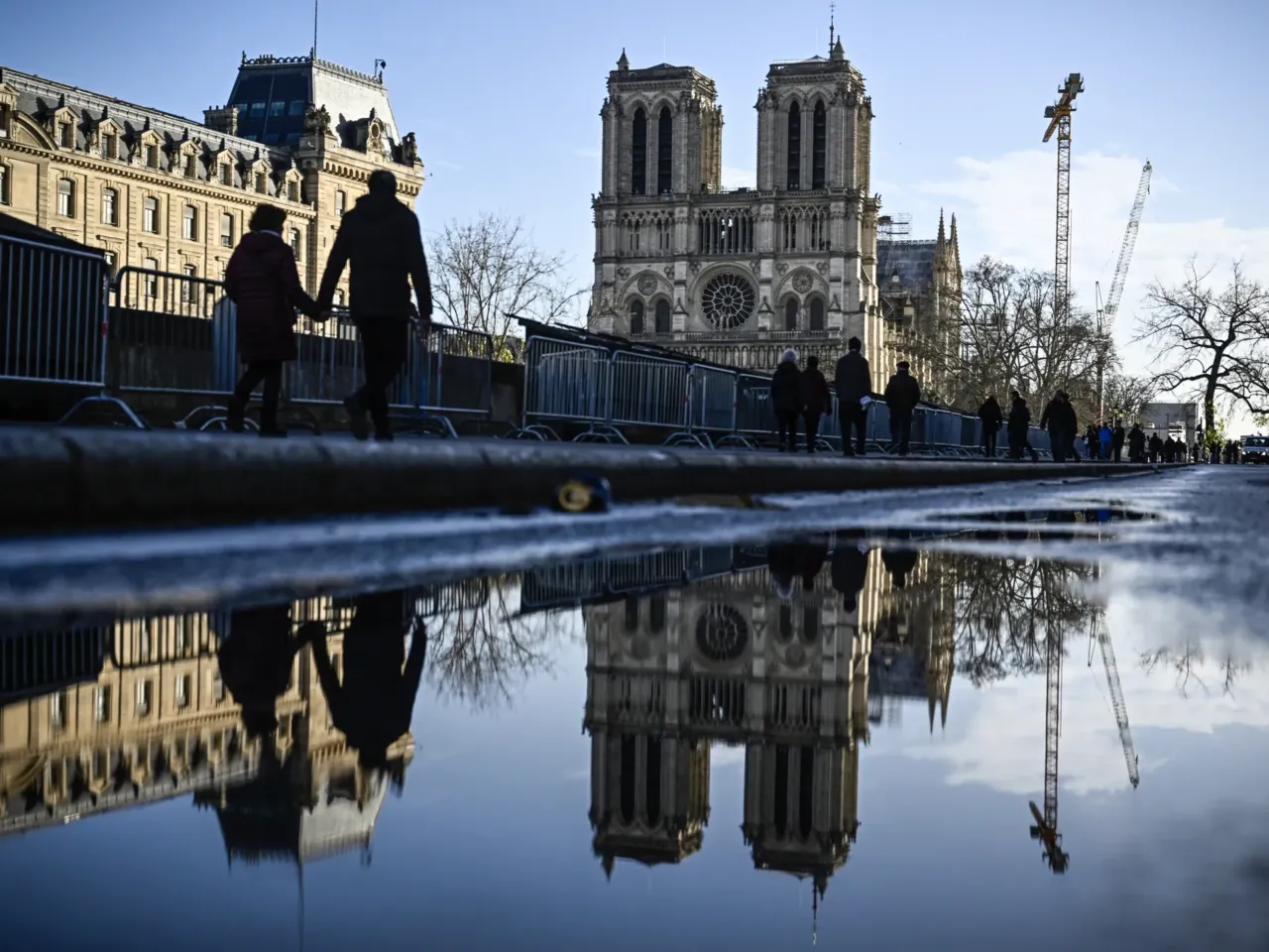 Pedestrians pass by the security barriers and fences placed around the Notre Dame Cathedral on the eve ahead of its official reopening, on Friday.