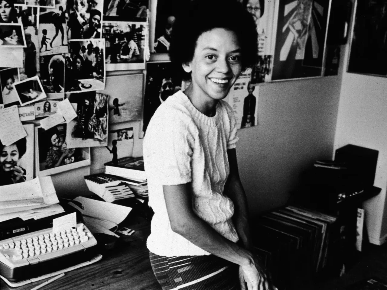 American poet Yolanda Cornelia 'Nikki' Giovanni leans on her desk beside a typewriter, in front of a wall decorated with photos, 1973. (Photo by Hulton Archive/Getty Images)