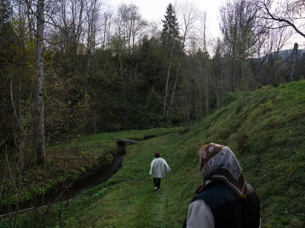 Olha Mys, wearing a fluffy wool hunia coat, and her sister walk near their house in Richka, Ukraine, down to where a valylo is built into the side of a stream. They use the valylo to wash wool and then to wash hunias for hours after they are woven.