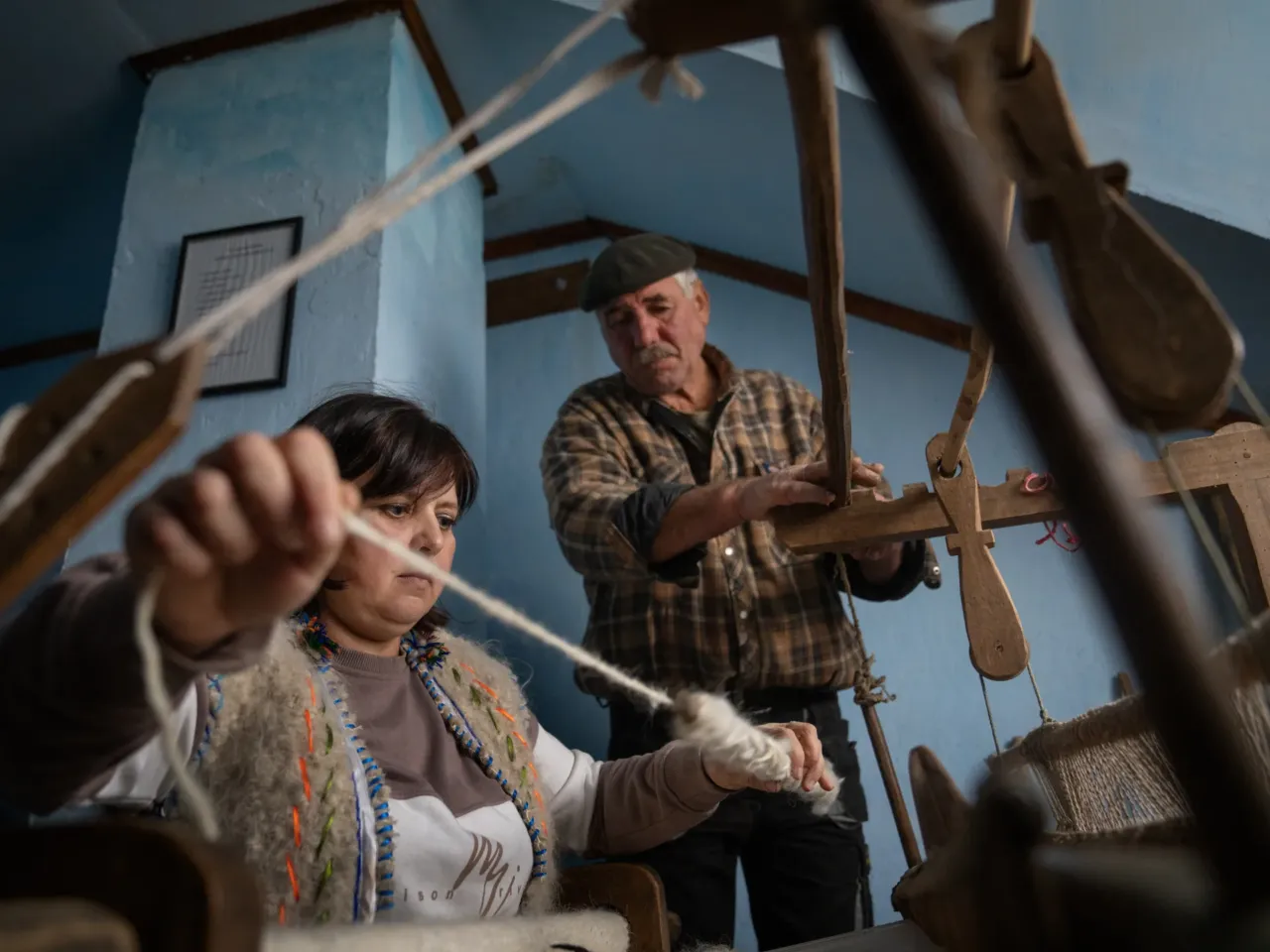 Lubov Hychka demonstrates how to weave the hunia fabric while Vasyl Hychka (unrelated), who takes care of the property where the loom is housed, helps with the rickety old machine.