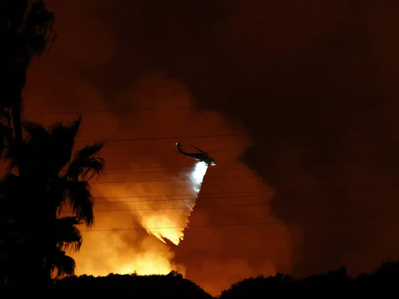 A firefighting helicopter drops water as the Palisades Fire burns toward the Mandeville Canyon neighborhood on January 10, 2025 in Los Angeles, California.