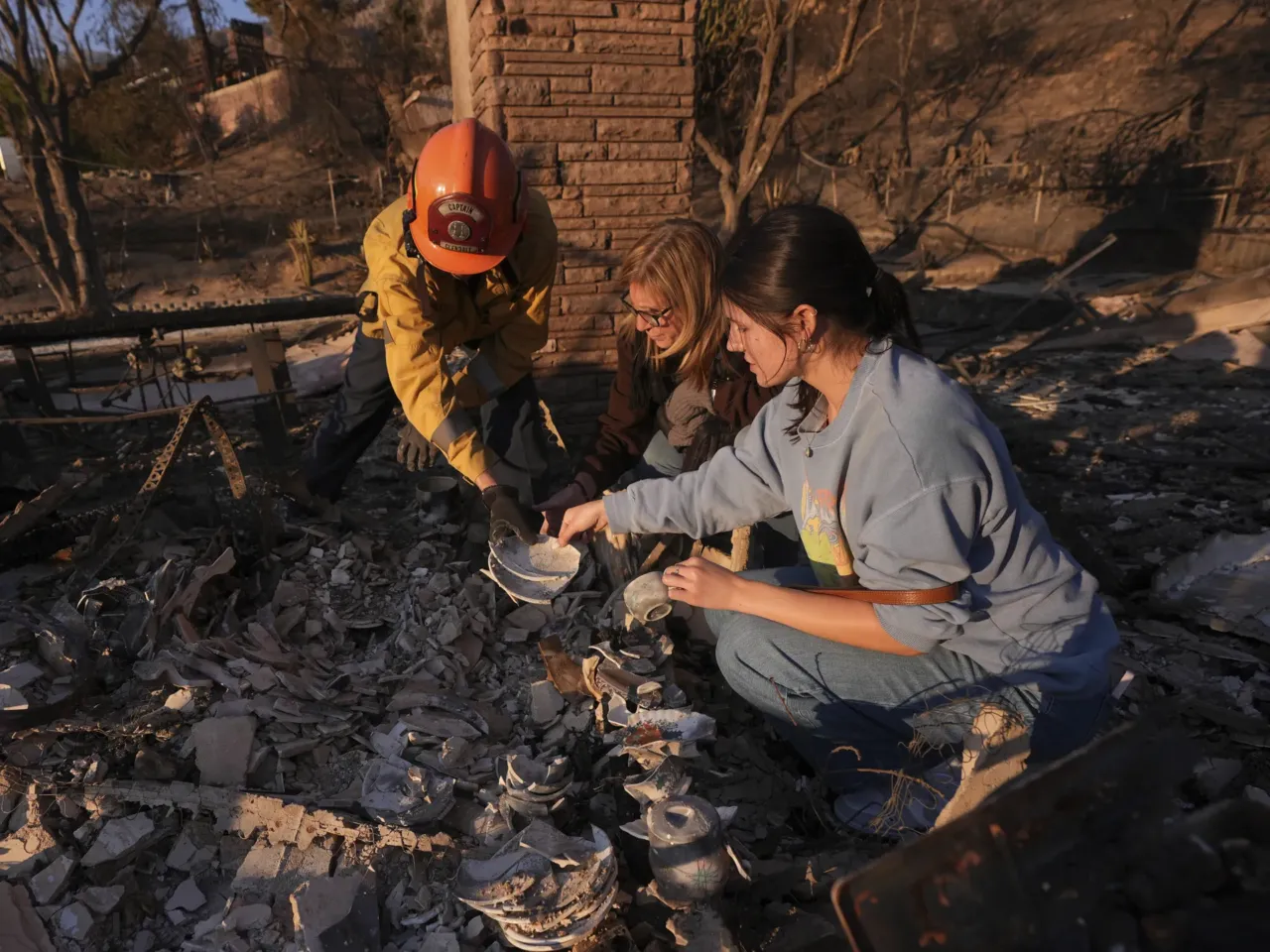 Saturday, Jan. 11: Glendale Fire Department captain Chris Jernegan (left) and his wife Alison (middle) help Ella Venne search through the remains of her family's home that was destroyed by the Eaton Fire in Altadena.