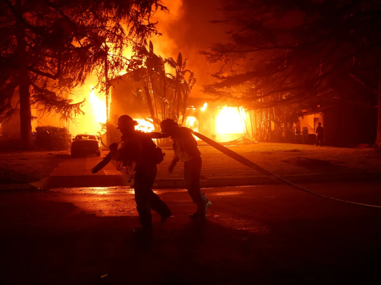 Los Angeles County firefighters pull a hose in front of a burning home as the Eaton Fire moved through the area in Altadena, Calif., on Jan. 8.