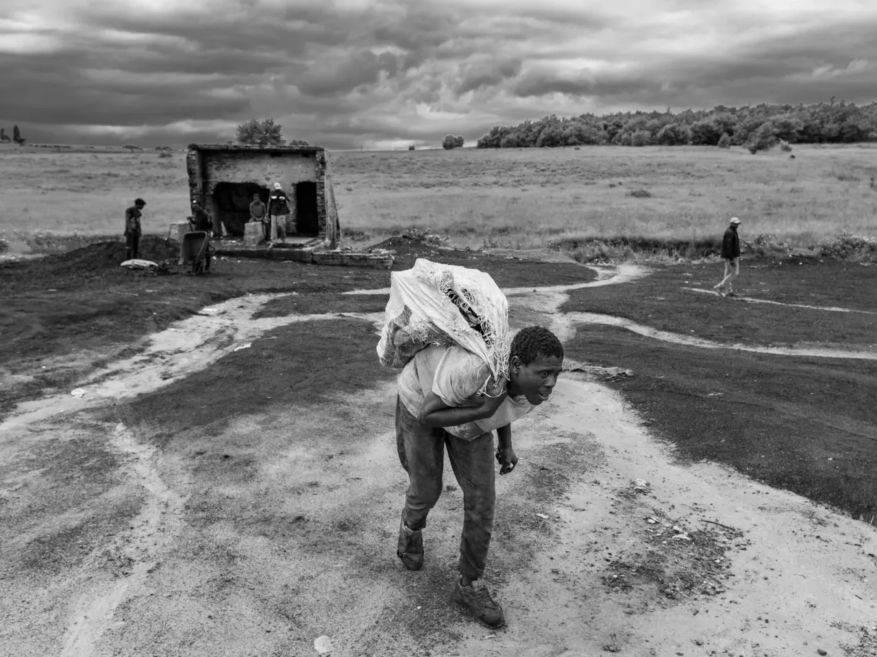 Artisanal coal miner Emmanuel Siyabonga hauls a sack of coal to a client's car at the abandoned Golfview coal mine in Ermelo, South Africa. The work is grueling and hazardous but is one of the few viable means of making a living in a town with widespread poverty and high rates of unemployment.