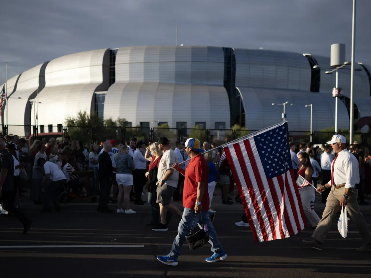A man carries a U.S. flag as people arrive for the public memorial service of right-wing activist Charlie Kirk at State Farm Stadium in Glendale, Ariz., on Sunday.