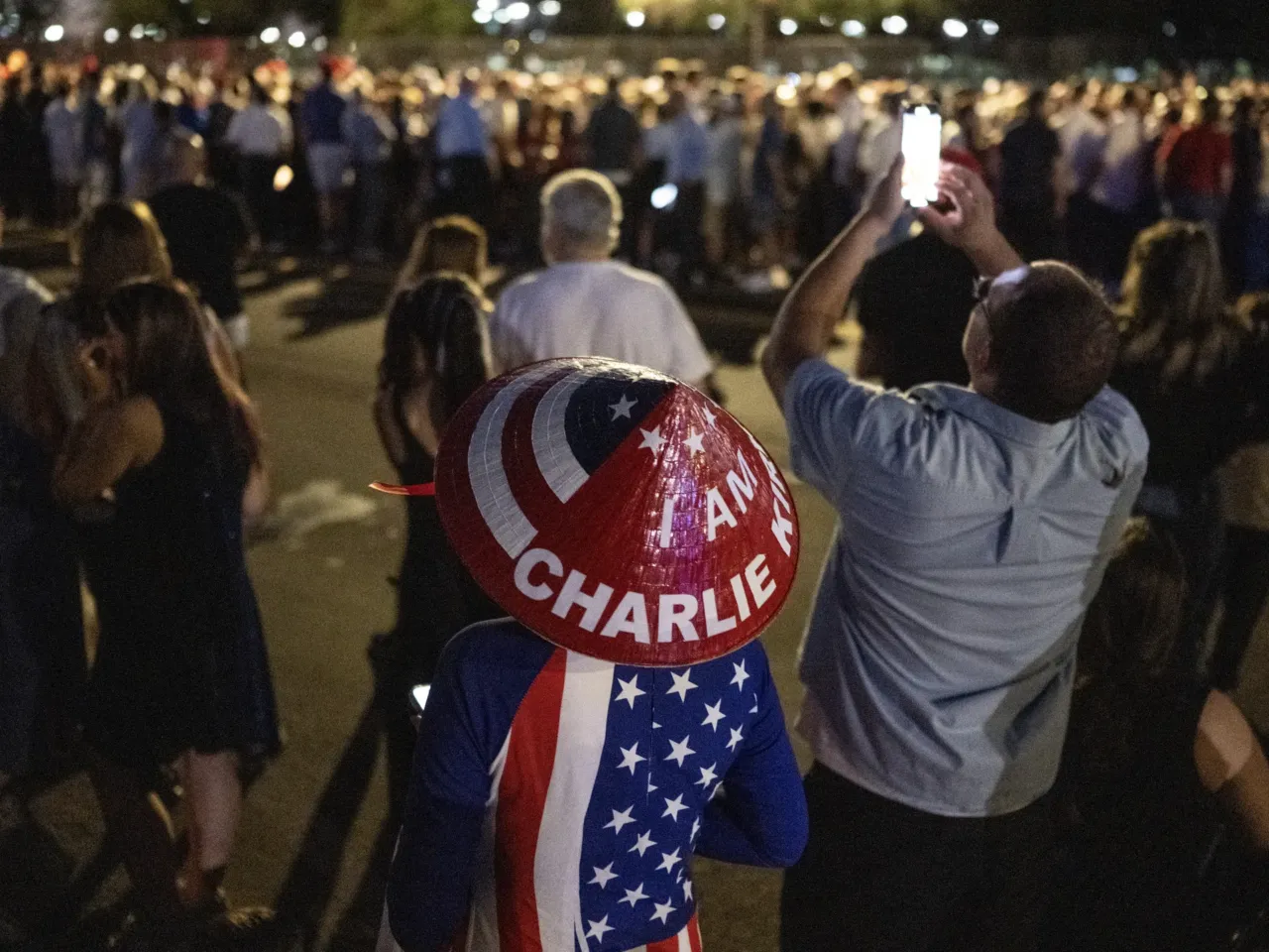 A person wears a hat reading "I am Charlie Kirk" as people arrive outside State Farm Stadium to attend Kirk's memorial.