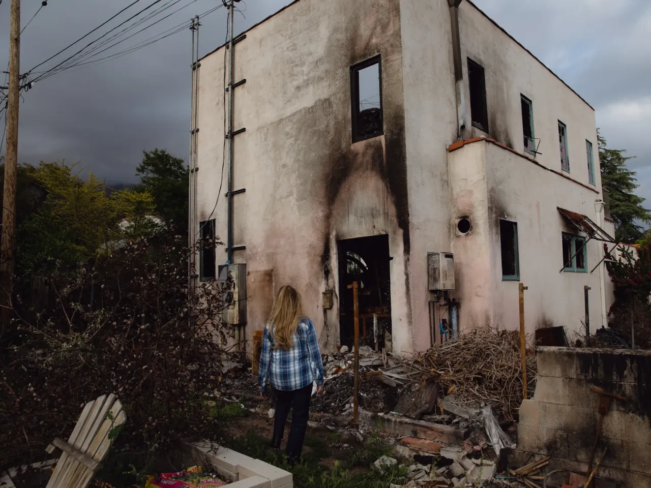 5 takeaways from NPR's investigation into the role of distribution lines in LA fires 1 Lea Chazin stands beside the remains of a building behind her home that was destroyed by the Eaton Fire.