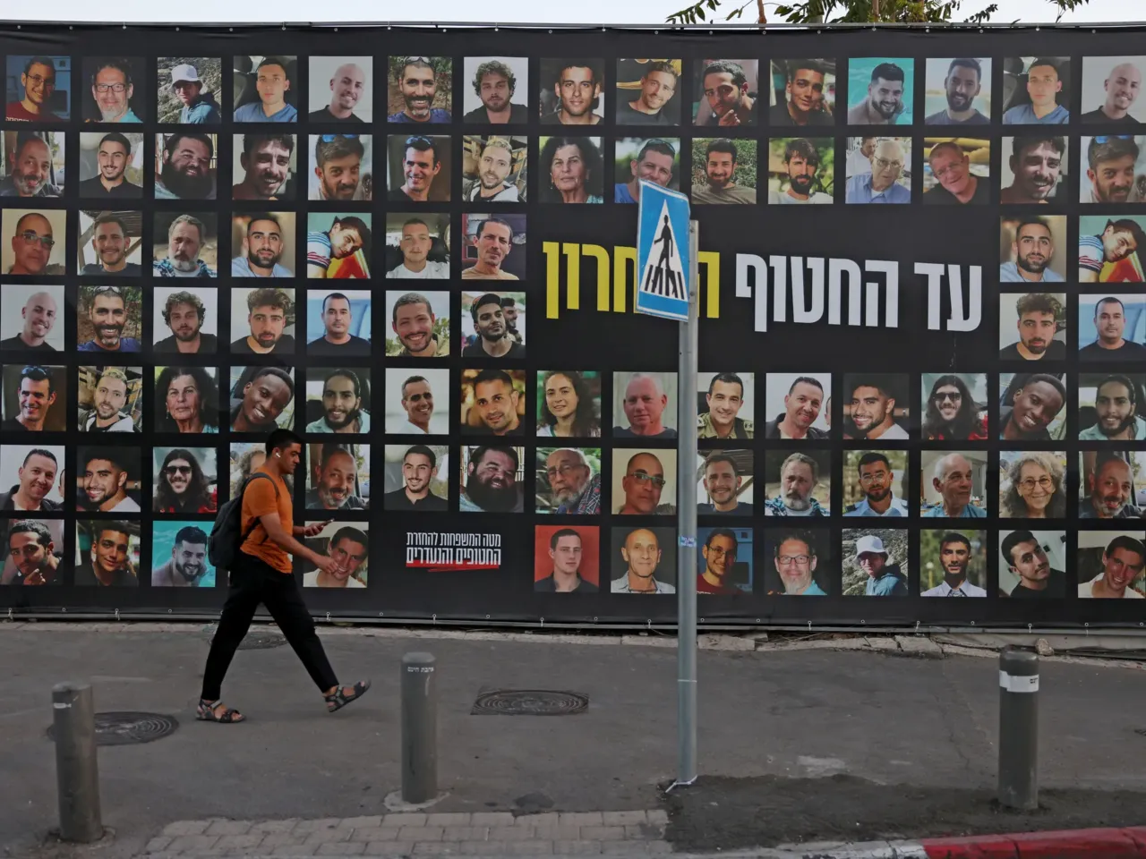 A man walks past a billboard bearing the portraits of Israelis held hostage in the Gaza Strip by Palestinian militants since Oct.2023.