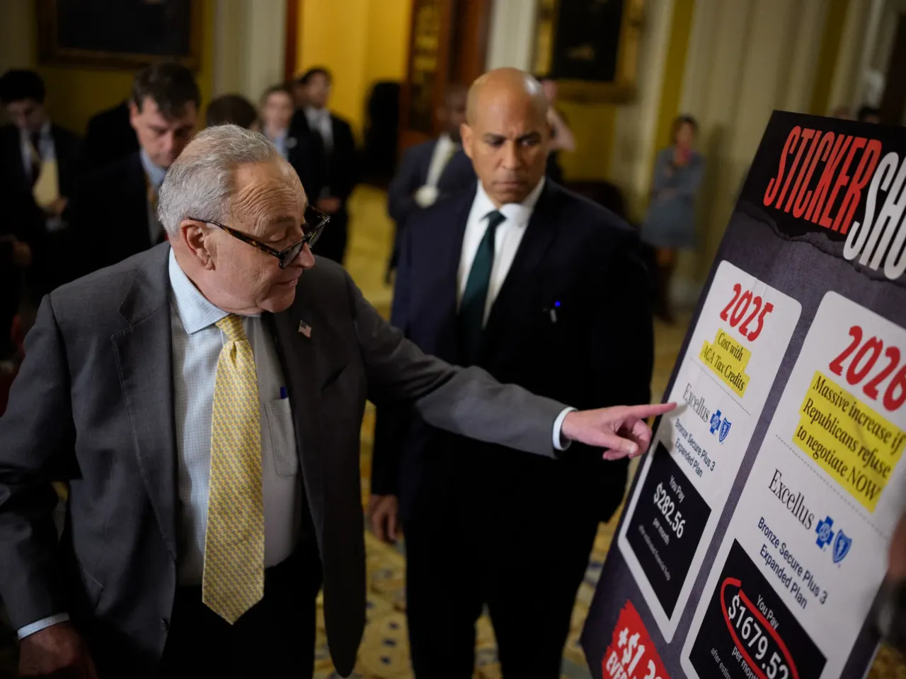 Senate Minority Leader Chuck Schumer, D-N.Y., accompanied by Sen. Cory Booker, D-N.J., points to a poster depicting rising medical costs if Congress allows the Affordable Care Act tax credits to expire as he speaks to reporters at the U.S. Capitol on Oct. 15, 2025.