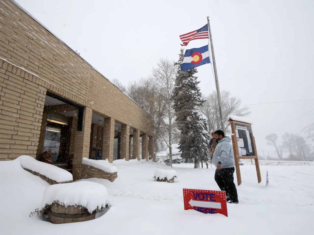 A voter carries his son as he walks into the Oak Creek Town Hall to drop off his ballot on Election Day, Nov. 5, 2024, in Oak Creek, Colo.