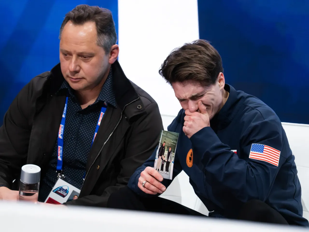 Maxim Naumov (right) holds a photo of his parents while he waits for his scores after competing in the men's short program competition during the 2026 U.S. Figure Skating Championships at the Enterprise Center on Thursday, Jan. 8, 2026, in St. Louis. It was his first nationals since his parents were killed last year when an American Airlines regional jet collided with a U.S. Army Blackhawk helicopter over the Potomac River. Maxim would go on to win the bronze medal in the men's finals.
