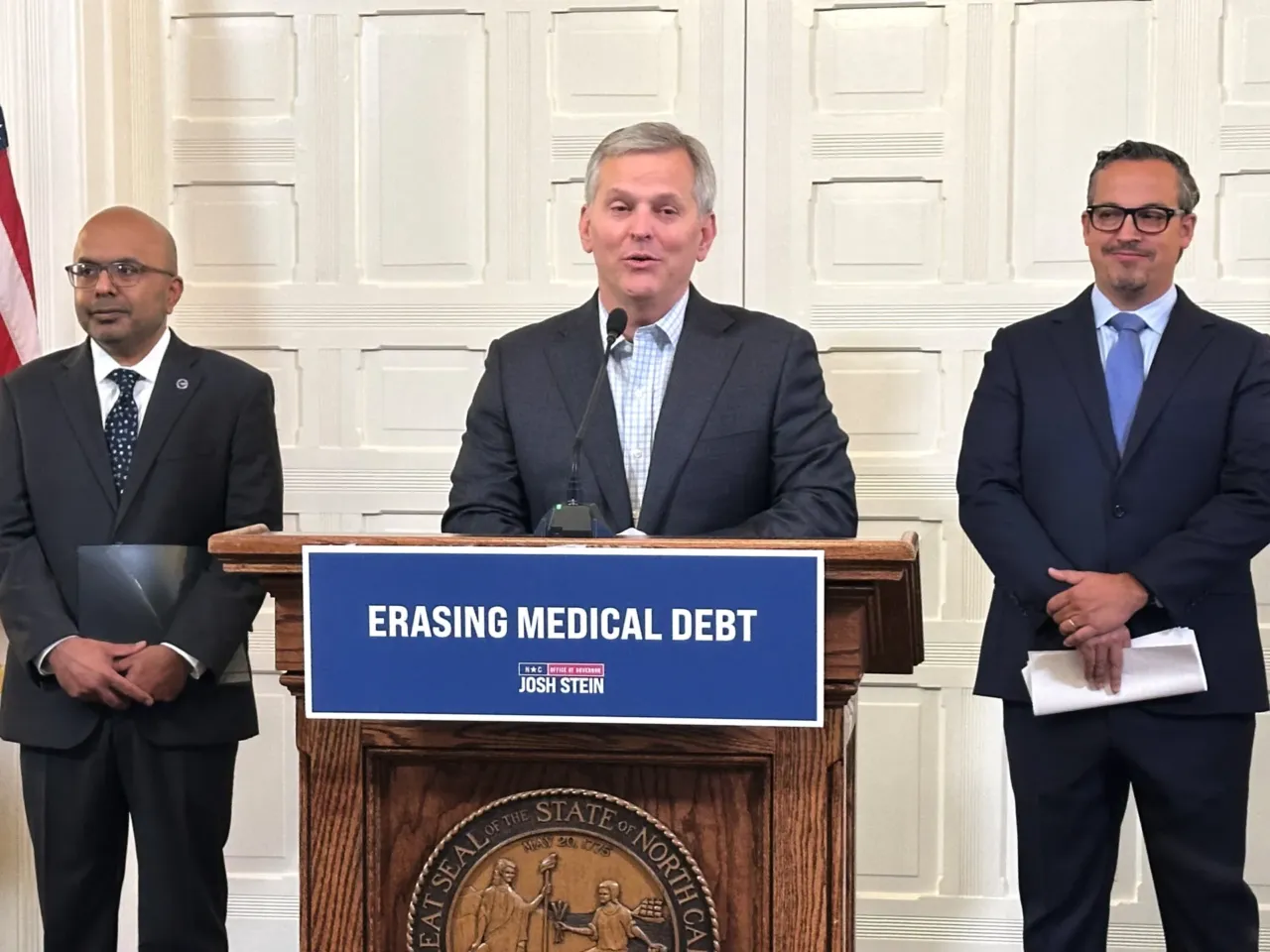 North Carolina Gov. Josh Stein (center), flanked by the state's health secretary, Dr. Dev Sangvai (left) and an executive from Undue Medical Debt, Jose Penabad, speaks about the elimination of medical debt through an initiative involving hospitals and Medicaid in Raleigh, N.C.