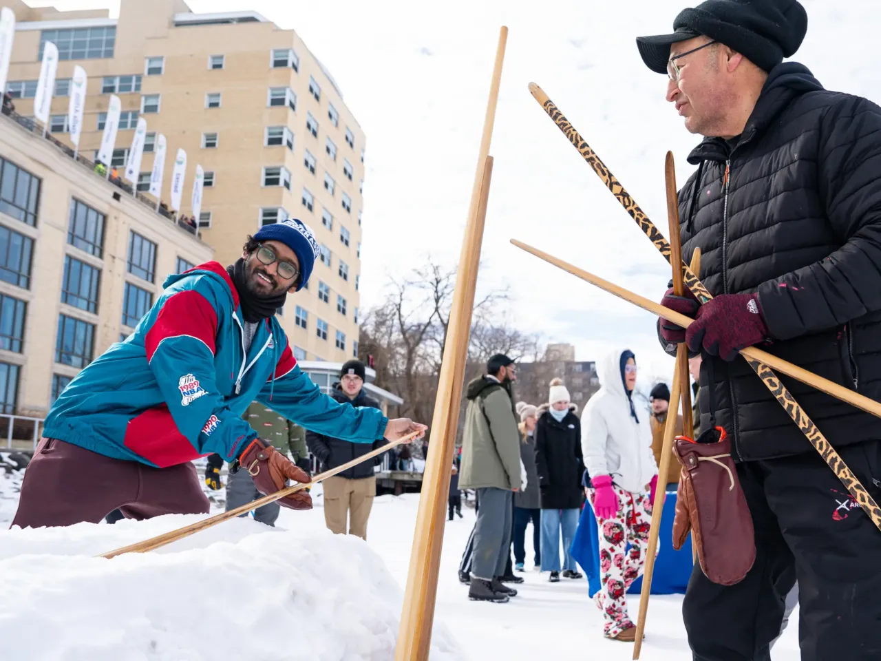 This community festival embraces the joys of a frozen lake — while it still has one 6 Bill Quackenbush, of Ho-Chunk Nation (right), teaches Praneeth Kolli (left) how to compete in the snow snake competition during the city's annual Frozen Assets Festival on Lake Mendota. Snow snake is a traditional Indigenous winter sport where players slide handcrafted wooden sticks down a trench made of snow for distance.