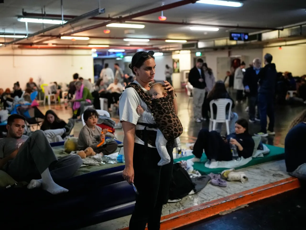 Leah Guttmann holds her son, Teddy, as other people take shelter in an underground parking garage while air-raid sirens warn of incoming missiles launched by Iran toward Tel Aviv, Israel, Sunday, March 1, 2026.