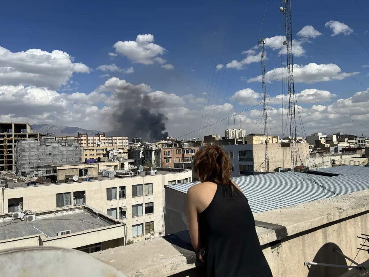 A person watches as plumes of smoke rise over the skyline following explosions on March 1, 2026 in Tehran, Iran.