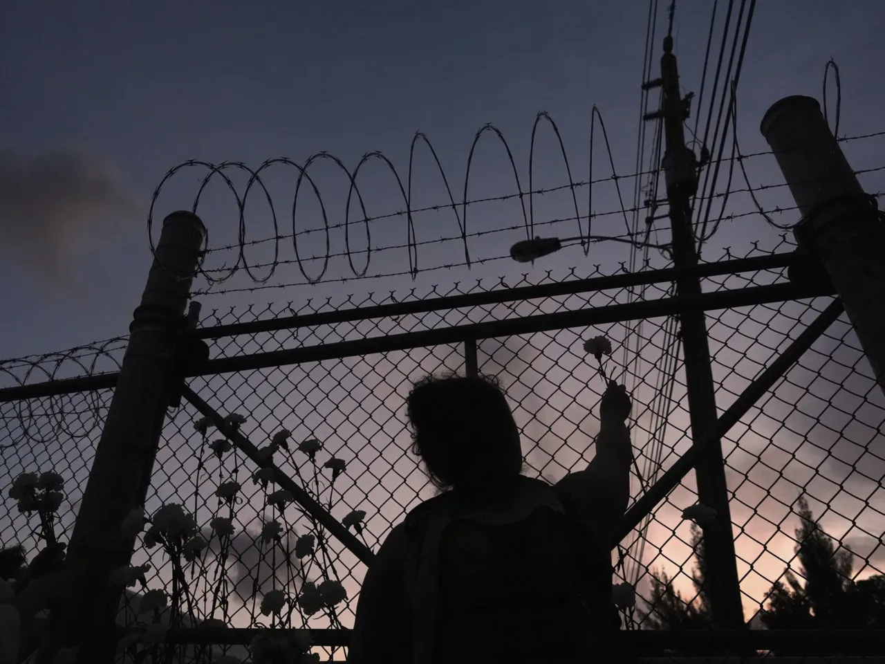People place flowers on a fence outside Krome Detention Center in Miami in May 2025, during a vigil to recognize people who have died in U.S. Immigration and Customs Enforcement custody as well as those affected by mass deportations.