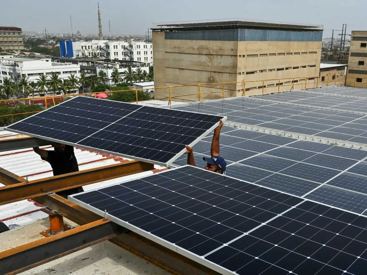 In this photograph taken on July 2, 2025, technicians install solar panels on the rooftop of a factory in Karachi, Pakistan.