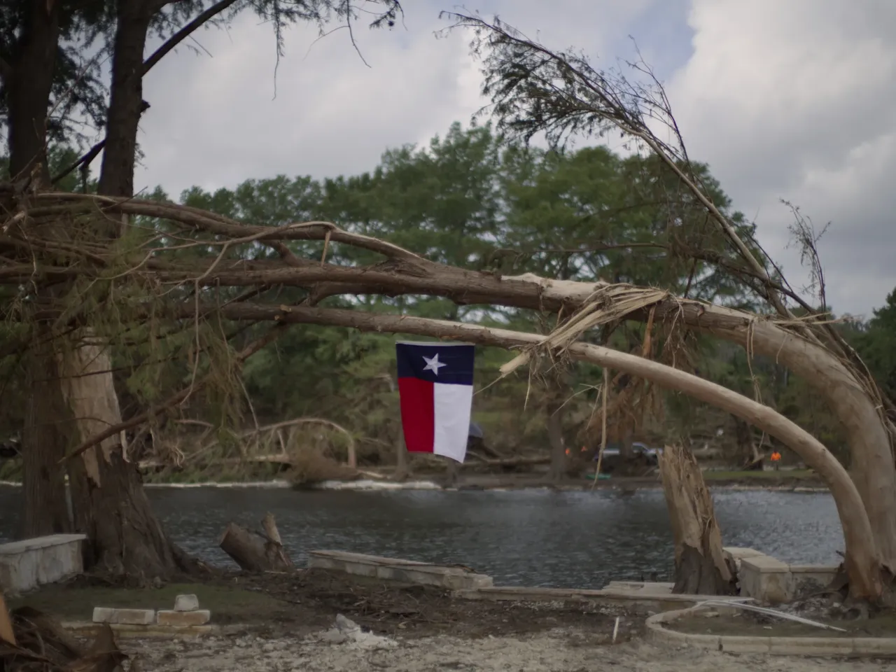 A Texas flag hangs from a flood-damaged tree on the bank of the Guadalupe River in Kerrville, Texas after deadly floods in July 2025. A group of emergency experts appointed by President Trump is recommending that the Federal Emergency Management Agency (FEMA) provide less money to states to help prepare for and respond to disasters including floods.