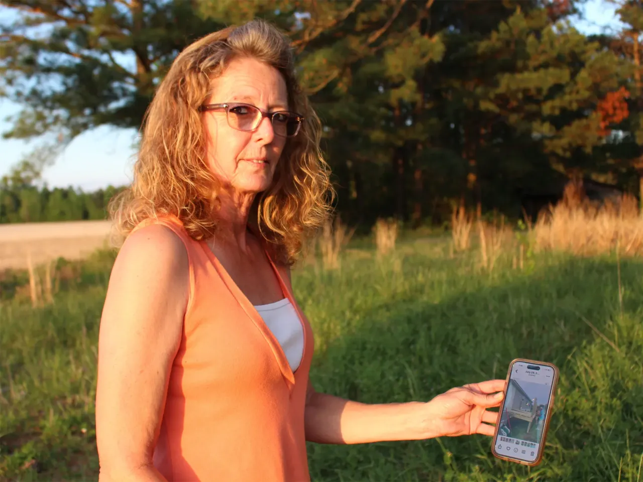 Debra Pierce holds up a picture of Stanley Sears, her brother, while standing in the yard of the mobile home he was renovating before his death in 2024. Pierce believes North Carolina's Martin County needs higher-level emergency services and a hospital.