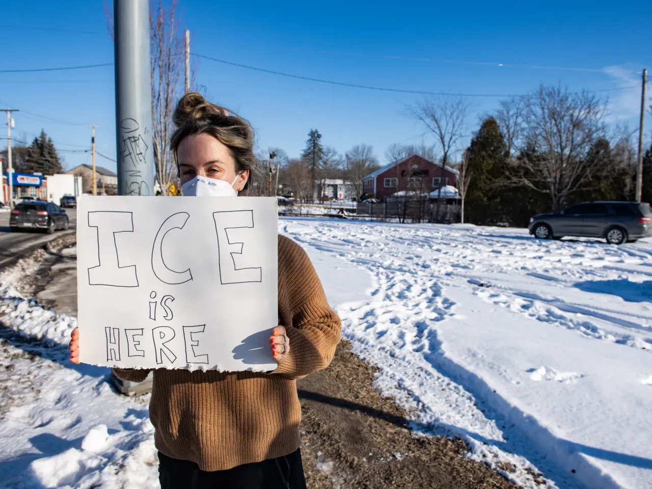 An activist stands outside across from what appears to be an U.S. Immigration and Customs Enforcement SUV in Portland, Maine on January 23, 2026.