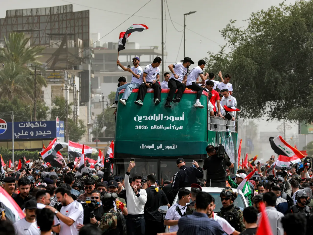 Members of the Iraqi men's national football team sit atop a double-decker bus are cheered on by the fans in the Jadriya area of central Baghdad on April 4, 2026. They were celebrating the country's qualification for the 2026 FIFA World Cup.