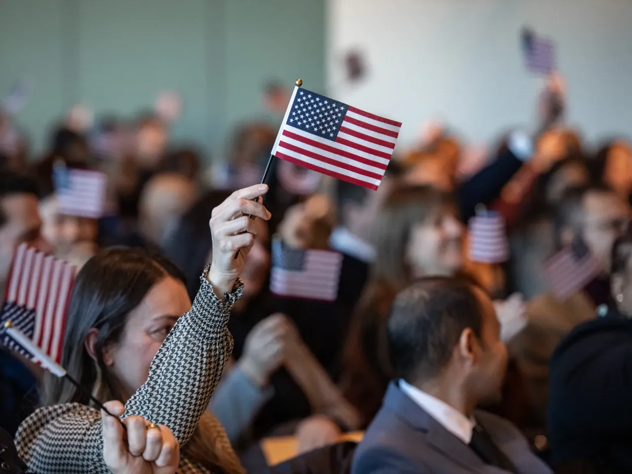 People wave U.S. flags to celebrate becoming U.S. citizens after taking the oath of allegiance during a naturalization ceremony in Boston in January 2025.