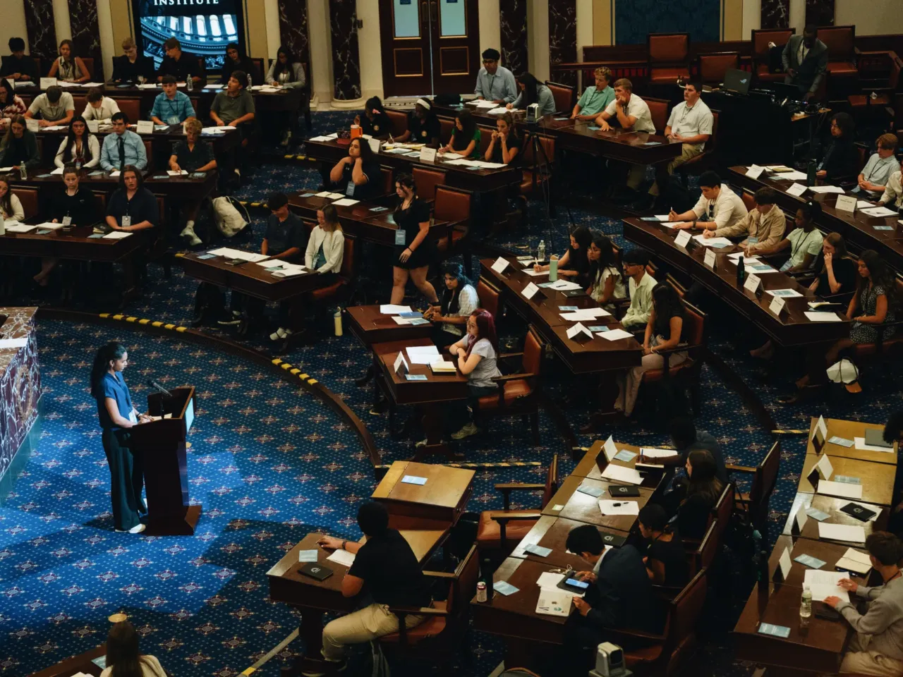 Students create AI policy at the Edward M. Kennedy Institute for the United States Senate in Boston. High school student Leena Jain of Louisiana addresses her fellow senators moments before the final vote.