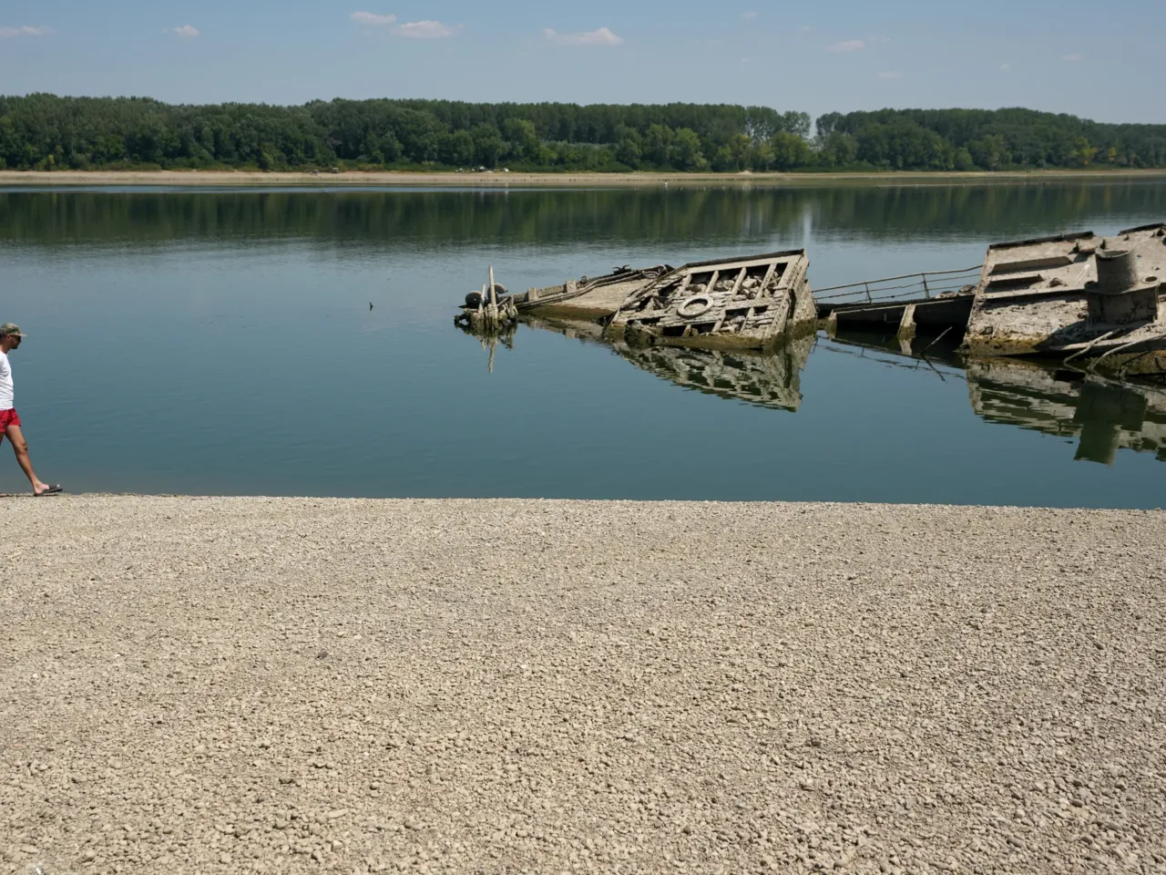 A man walks on a sandbank by the wreckage of a WWII German warship, which emerged during the drought in front of Djerdap II, a large dam on the Danube River between Romania and Serbia near Prahovo on Aug. 4, 2026.